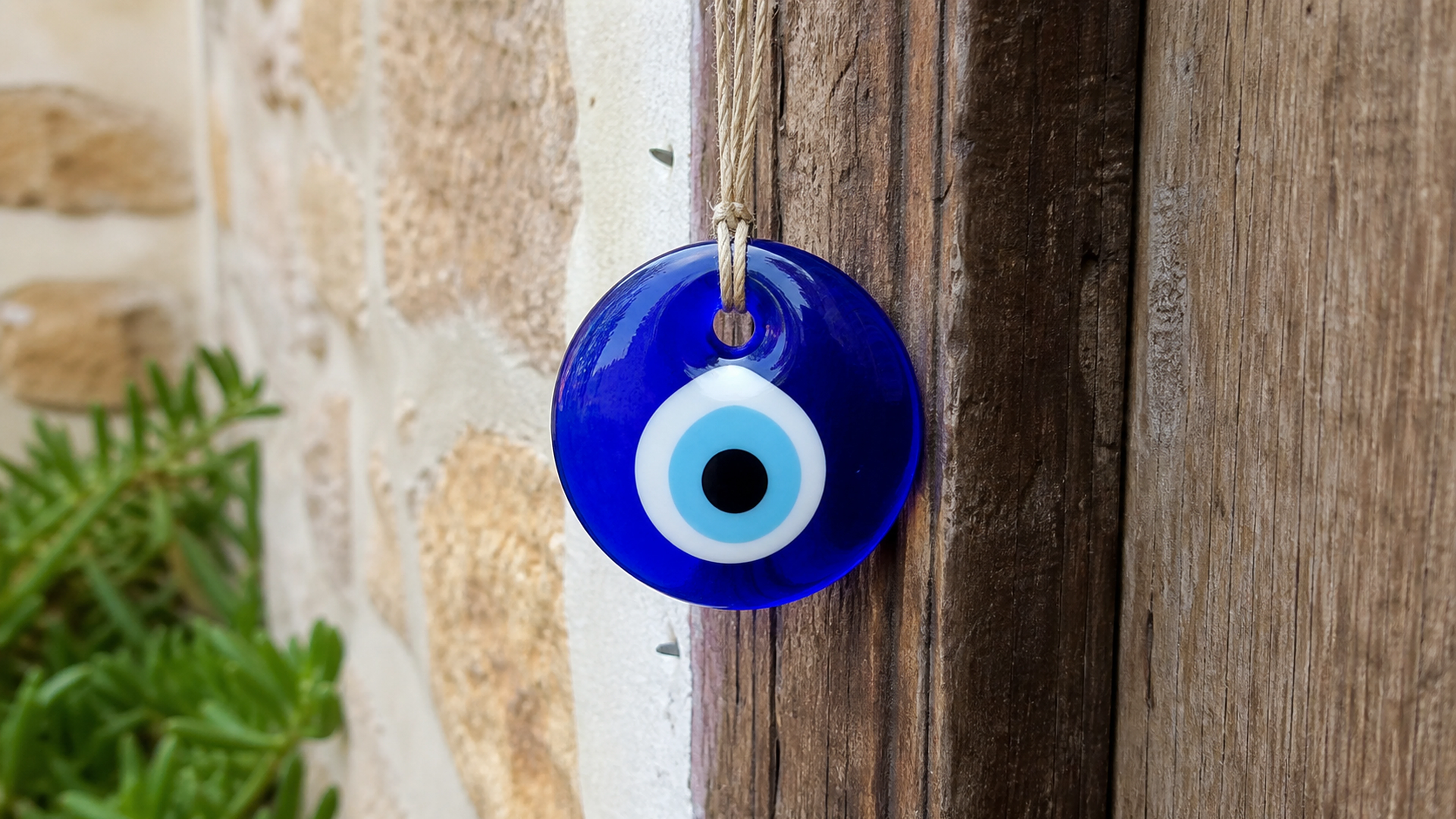 Amulette Nazar en verre bleu suspendue près d'une porte méditerranéenne en bois.