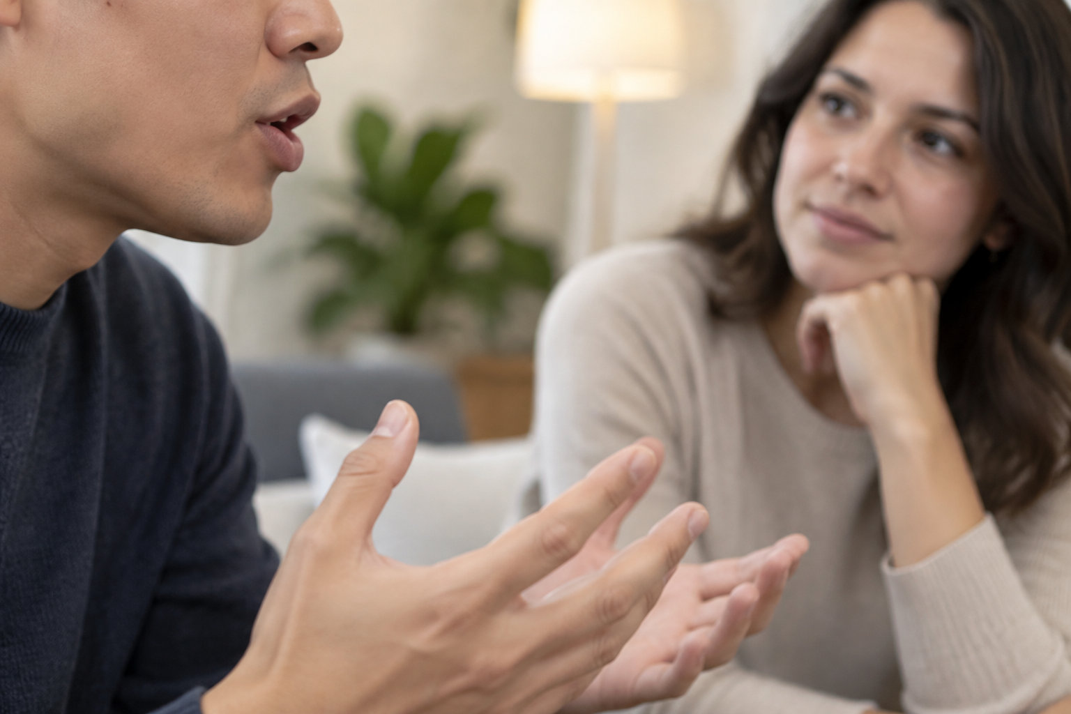 Un homme parle en gesticulant tandis qu’une femme l’écoute, le menton appuyé sur la main, dans un salon.